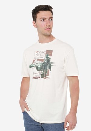 Cream-colored t-shirt featuring a graphic of a character in green with spaceship illustrations in the background. Short sleeves, cotton material.