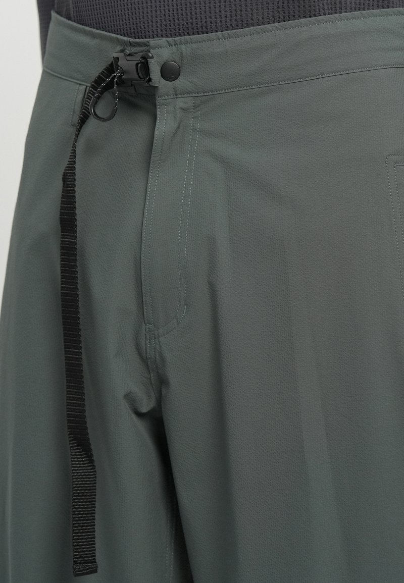 Pantalons de sport gris en tissu texturé avec taille à cordon de serrage et fermeture à bouton, dotés de poches latérales et d'un design à coupe décontractée.