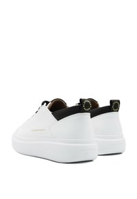Sneaker bianche con tomaia in pelle liscia, linguette sul tallone nere a contrasto, branding in rilievo e suola in gomma bianca spessa.