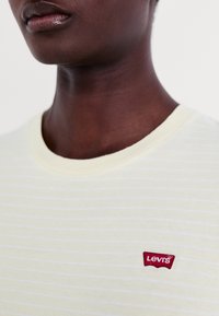 Żółty t-shirt z krótkim rękawem, z białymi poziomymi paskami i czerwonym naszywką z logo Levi's na piersi. Miękka bawełniana tkanina, okrągły dekolt.
