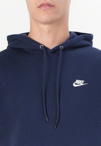 Camisola capuz azul marinho com cordão. Apresenta um pequeno logótipo branco da Nike no peito. Feita de um tecido macio e texturizado.