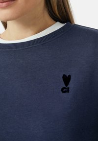 Marineblauwe sweatshirt met een ribbelkraag, voorzien van een zwart geborduurd hart en "ci" logo op de borst. Zachte stoftextuur.