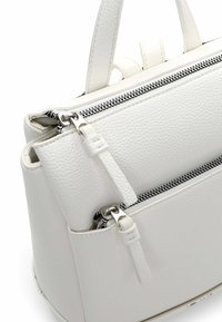 Valge tekstuuriga käekott, millel on hõbedased tõmblukud, kaks sektsiooni ja lühikesed sangad. Materjal on pehme ja krobeline.