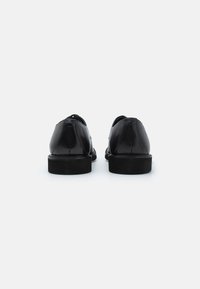 Zwarte leren schoenen met een ronde neus, een gladde afwerking en een lage rubberen zool. De achterkant toont een schone uitstraling met subtiele stiksels.