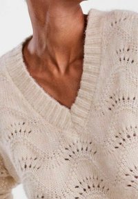 Sweter w jasnym beżowym kolorze z wełny, z dekoltem w serek, z falistym wzorem i prążkowanymi krawędziami, o miękkiej teksturze i delikatnymi ażurowymi detalami.