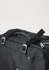 Black fabric bag with a textured surface, silver hardware, dual handles, and adjustable straps; features triangle accents and a zipper.