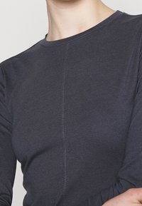 Mörkgrå långärmad skjorta i mjukt tyg. Rund halsringning, figursydd design med en mittsöm detalj. Slät textur, minimala accentdetaljer.