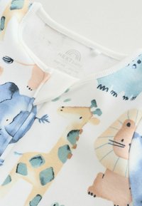 Biały kombinezon z tkaniny z kolorowymi nadrukami zwierząt, w tym żyrafy, lwa i słonia. Gładka faktura z kołnierzykiem w kształcie litery V.