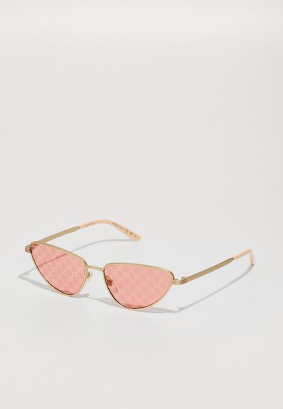 Pink cat-eye sunglasses with a patterned lens featuring a gold metal frame and light pink temples, showcasing a modern geometric design.