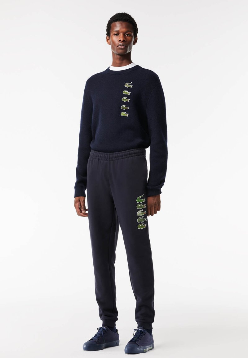 Pull marin avec des accents brodés verts, associé à un jogging assorti avec des détails similaires. Le pantalon possède une taille élastique.