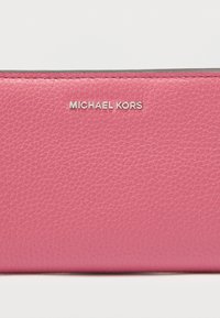 Ροζ δερμάτινο πορτοφόλι με υφή στην επιφάνεια. Εμβλητικό ασημί λογότυπο «MICHAEL KORS» στην πρόσοψη. Συμπαγής ορθογώνιο σχήμα.