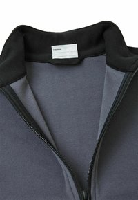 Szara polarowa kurtka z czarnym kołnierzem i zamkiem błyskawicznym. Miękka tekstura, z metką wewnątrz kołnierza do osobistej identyfikacji.