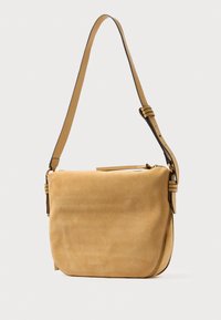 Tana nubuk torbica s kožnim remenom koji se može prilagođavati, zaobljenim dnom i bočnim patentnim zatvaračem na bijeloj pozadini.