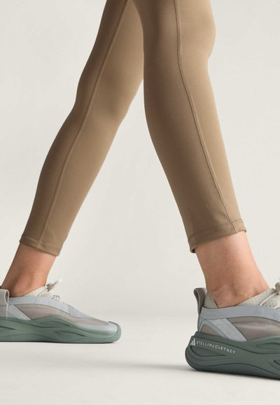 Beige sportovní legíny s plochými švy a délkou po kotníky. Šedé a mintové tenisky s vícevrstvými materiály a strukturální podrážkou.