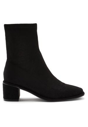 Bottine noire à talon carré, finition en daim lisse, avec une tige ajustée, semblable à un chausson, qui s'étend au-dessus de la cheville.