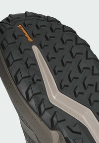 Svart gummiyttersula med djupa mönster och en beige mellansula. Utmärks av en "Continental"-logotyp i orange, vilket förbättrar greppet och tractionen.