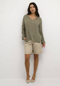Ljusgrön långärmad topp med v-ringning och sidofickor, matchad med beige knälånga shorts. Mjukt tyg med en lös passform.