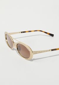 Kuldprillid ovaalsete läätsedega, pruunikate toonidega, ja tekstuuriga raami, millel on rhinestone aktsendid. Muster tortoise shell'i templid.