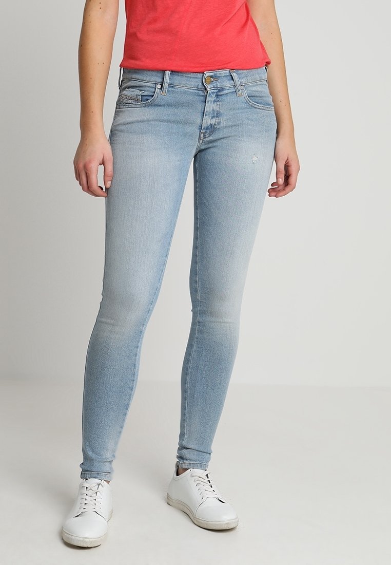 Jeans ajustados de color azul claro con un acabado desgastado, diseño de cinco bolsillos y cierre de botón metálico, combinados con zapatillas blancas.