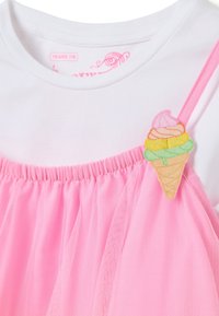Witte blouse met een roze tule overlay, voorzien van een sprankelende ijshoorntje als versiering op de schouder. Zachte stof, comfortabele pasvorm.