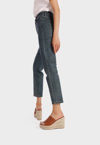 Jeans in denim scuro con gamba dritta, abbinati a sandali con zeppa marroni dotati di una piattaforma in espadrille testurizzata.