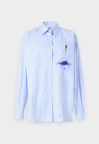 Camicia button-up azzurra in cotone con maniche lunghe, caratterizzata da una macchia di colore blu scuro sul lato sinistro e una tasca sul petto con una penna.