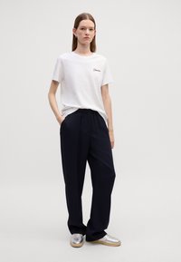 Biała bawełniana koszulka z haftowanym tekstem, w połączeniu z luźnymi granatowymi spodniami i srebrnymi sneakersami. Prosty design i neutralne kolory.