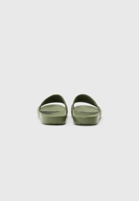 Infradito in gomma verde con retro aperto, cinturini curvi e suole interne testurizzate. Il design presenta un materiale liscio e flessibile senza decorazioni.