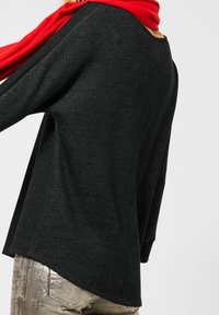 Mörkgrå, texturerad tröja med vida ärmar och rundad halsringning, ihopparad med glänsande metalliska byxor och en lysande röd scarf som hänger över.