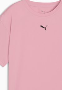 Světle růžové tričko s krátkým rukávem, vyrobené z hladkého materiálu, s černým logem Puma na hrudi, kulatým výstřihem a uvolněným střihem.