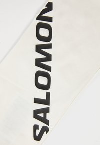 Tessuto bianco con grandi lettere nere che spellano "SALOMON" stampate verticalmente.