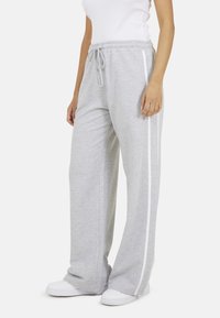 Grijze sweatpants van zacht materiaal met een losse pasvorm, voorzien van witte zijkanten. Elastische tailleband met trekkoord voor een verstelbare pasvorm.