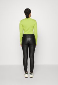 Top de manga larga verde acanalado y pantalones ajustados de cuero sintético negro. Los pantalones tienen bolsillos y un diseño ajustado. La modelo está de espaldas a la cámara.