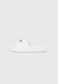 Λευκό λαστιχένιο σανδάλι τύπου slide με πράσινο λογότυπο κροκοδείλου στο λουράκι. Ομαλή υφή με επίπεδη σόλα. Απλός, μίνιμαλ σχεδιασμός.