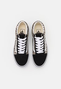 Une paire de baskets noir et blanc avec des motifs de pelage animal et des lacets blancs sur fond blanc.