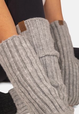 Ben iført høje, ribstrikkede grå benvarmere med brune lædermærker, kombineret med sorte leggings.