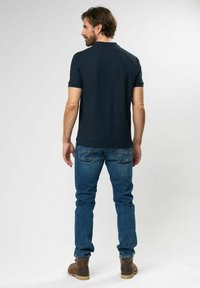 Navy polo t-shirt, kortærmet, båret med blå jeans og brune støvler. Casual pasform, glat tekstur, enkelt design og ingen synlige mønstre.