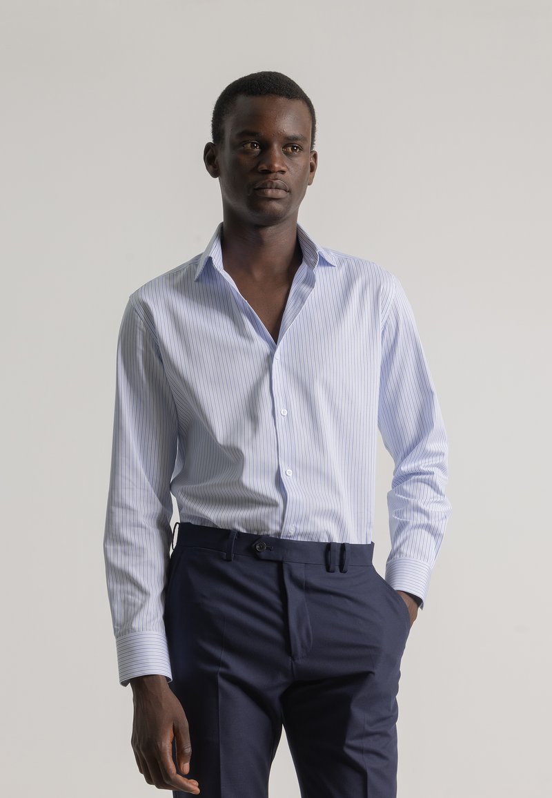 Camisa de vestir a rayas de color azul claro con cuello extendido, mangas largas y botones en la parte delantera, combinada con pantalones navales ajustados.