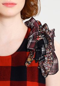 Bluse im roten und schwarzen Karo mit einem rüschendetail aus Stoff, das florale und karierte Muster an der Schulter aufweist, mit strukturiertem und geschichtetem Design.