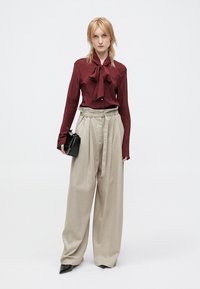 Blouse en bourgogne avec un nœud papillon, pantalon large gris, et petit sac à main noir. Tissu lisse et coupe ajustée.