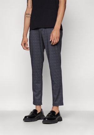 Dunkelgraue strukturierte Hose mit kariertem Muster, kombiniert mit eleganten schwarzen Schuhen mit einer Schnallendetail.