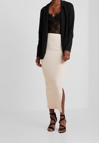 Czarna marynarka o dopasowanym kroju, zestawiona z czarnym koronkowym body i kremową spódnicą midi z bocznym rozcięciem, uzupełniona czarnymi sandałami na obcasie.