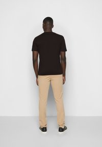 Černé tričko s krátkým rukávem, béžové slim-fit kalhoty, černé tenisky, zobrazené zezadu na jednoduchém bílém pozadí.