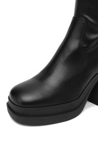 Černá kožená kotníková bota s kulatou špičkou, masivní platformou a mírným podpatkem. Hladký povrch s minimem švů.