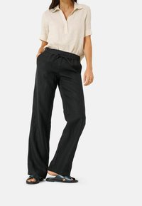 Czarne, lekkie, szerokie spodnie z elastycznym pasem, zestawione z beżową, krótko rękawową koszulą z kołnierzykiem z lnu i ciemnymi sandałami.
