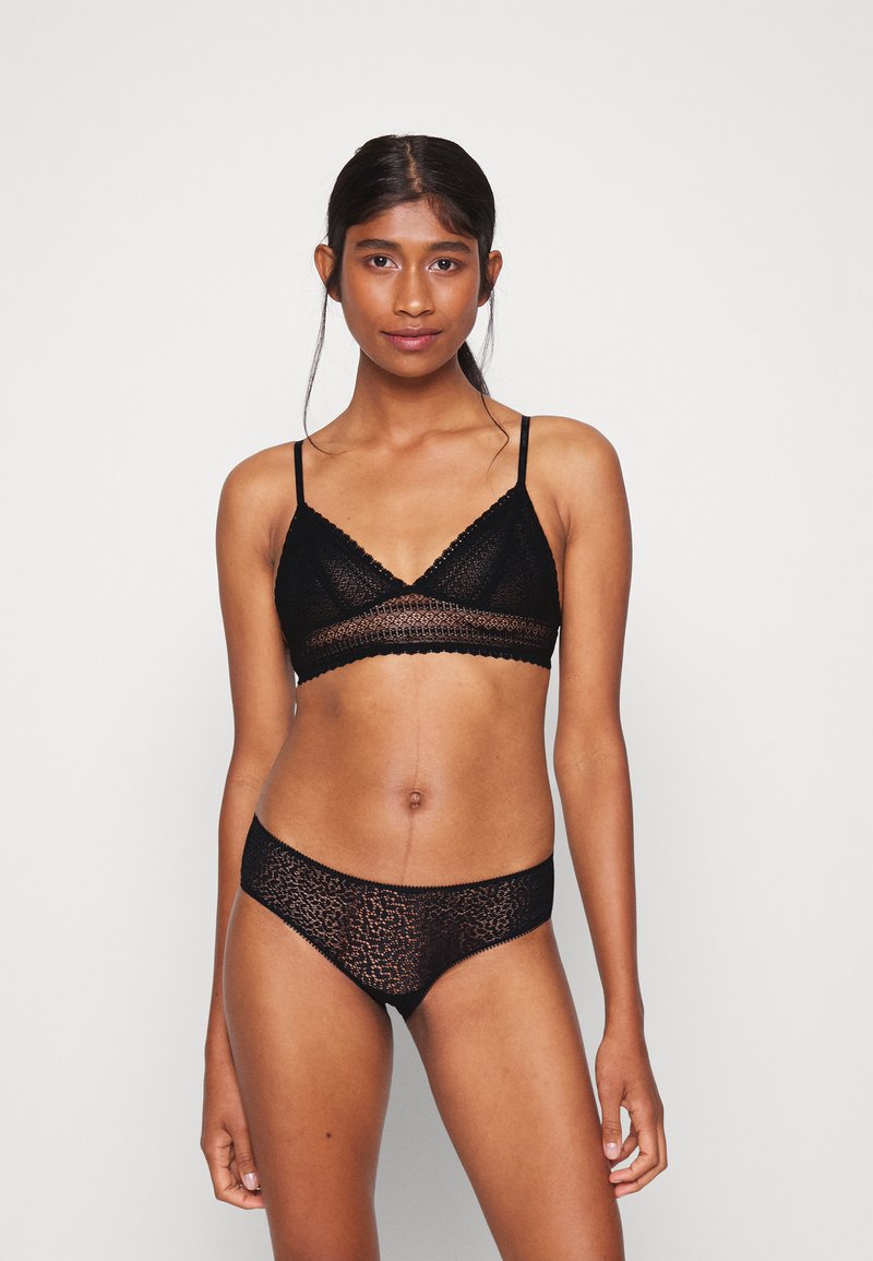 Bralette in pizzo nero dalla forma triangolare e con spalline sottili, abbinata a mutandine in pizzo coordinate con motivo leopardato e bordi scallop.
