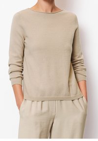 Helle beigefarbene Strickjacke mit rundem Halsausschnitt, langen Ärmeln, gerippten Bündchen und lässiger Passform. Hergestellt aus weichem, strukturiertem Stoff.