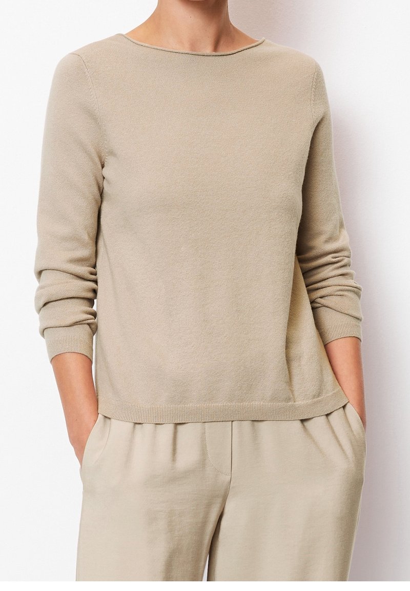 Helle beigefarbene Strickjacke mit rundem Halsausschnitt, langen Ärmeln, gerippten Bündchen und lässiger Passform. Hergestellt aus weichem, strukturiertem Stoff.