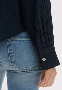 Navy textured shirt with long sleeves, featuring a buttoned cuff, paired with light blue denim jeans with a classic pocket design.