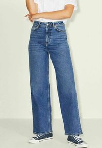 Jean en denim bleu taille haute avec une coupe large, dotée de poches avant et de surpiqûres en contraste. Associé à des baskets blanches.